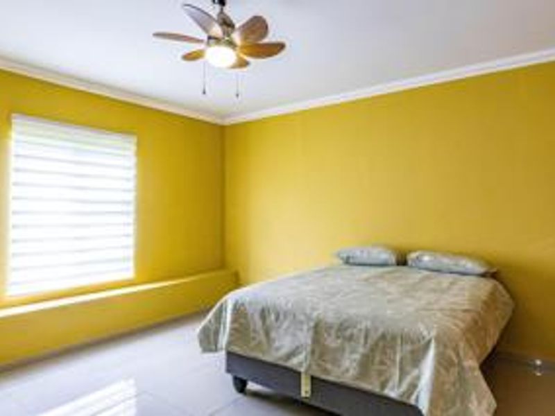 A bedroom featuring tiled flooring, a ceiling fan, and roller blinds, finished with yellow wall paint and decorative cove molding.