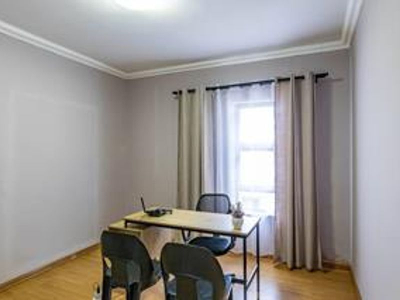 A functional office space featuring laminate flooring, neutral wall tones, and a window with curtains, providing a bright and versatile work environment.