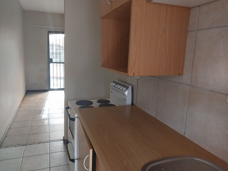 A functional kitchen featuring tiled flooring, laminate countertops, and built-in cabinetry, leading to a secure exterior entrance.