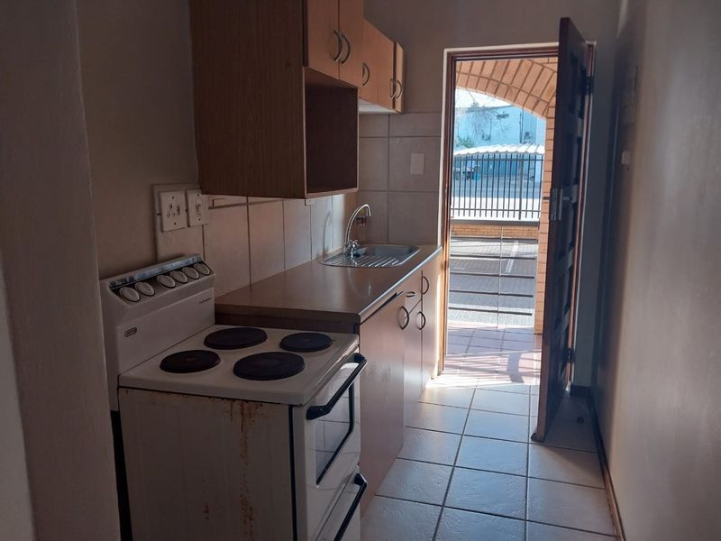 Compact kitchen featuring built-in cabinetry, a stainless steel sink, tiled backsplash, and direct access to an outdoor area.