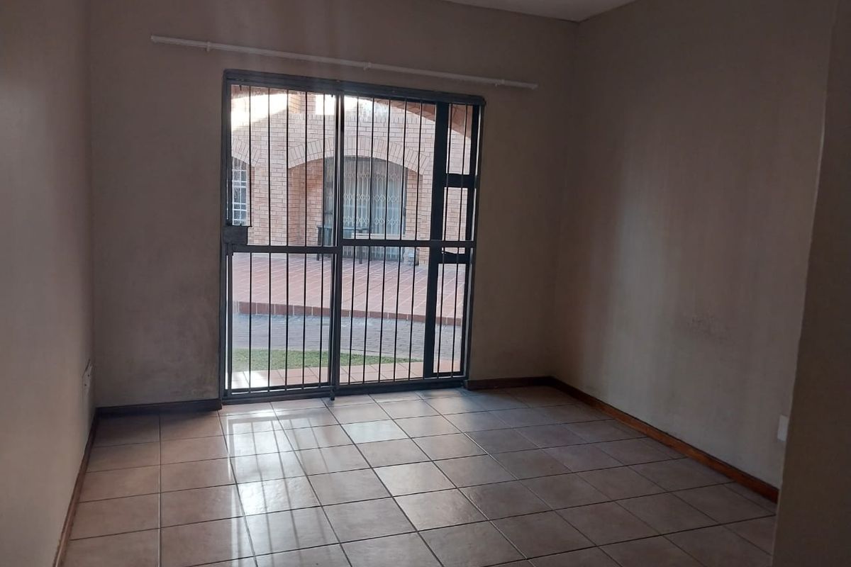An empty living room featuring tiled flooring and a sliding glass door with a security gate, leading to an outdoor patio area.