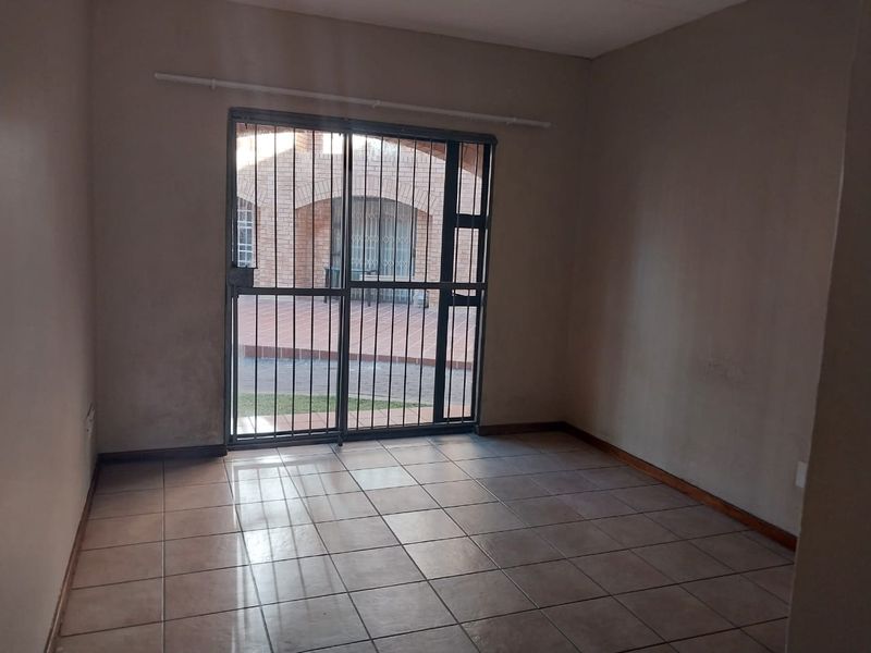 An empty living room featuring tiled flooring and a sliding glass door with a security gate, leading to an outdoor patio area.