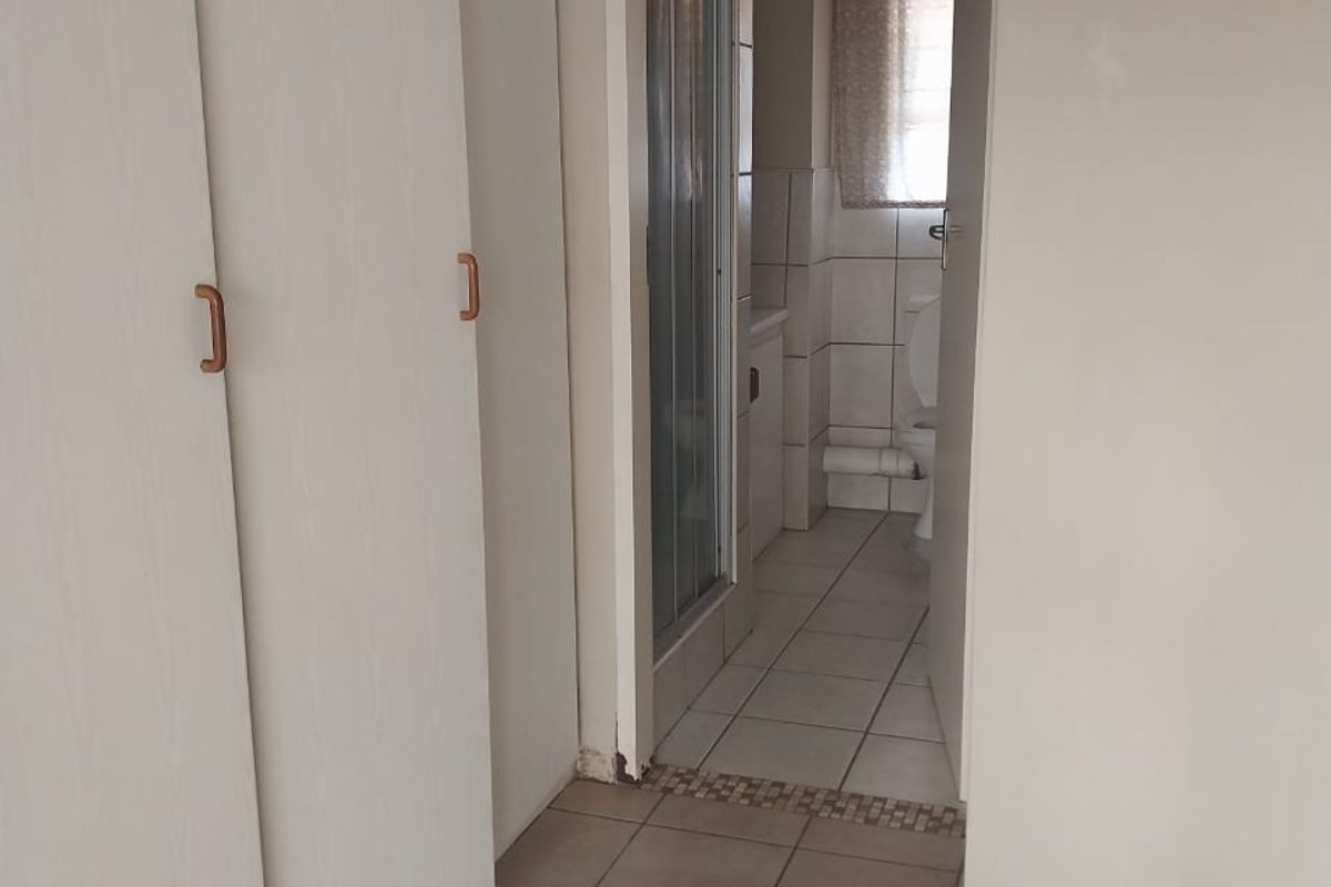 A functional hallway featuring built-in cupboards and tiled flooring, providing direct access to an adjoining bathroom with a shower and toilet.