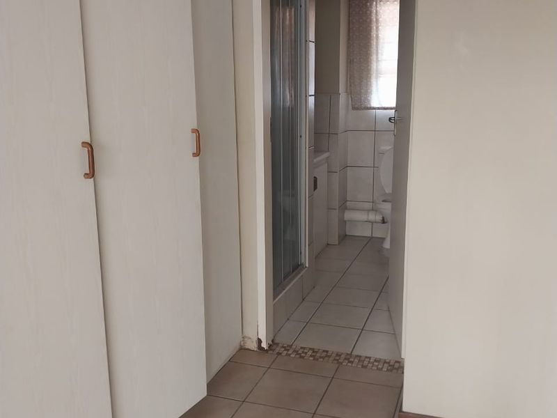 A functional hallway featuring built-in cupboards and tiled flooring, providing direct access to an adjoining bathroom with a shower and toilet.
