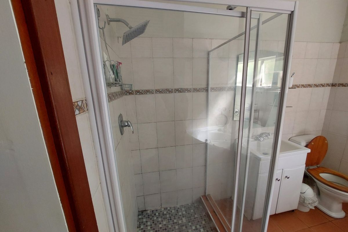 A functional bathroom featuring a glass-enclosed shower with mosaic flooring, a vanity basin, and a standard toilet, finished with tiled walls.