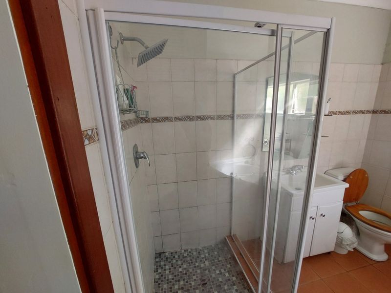 A functional bathroom featuring a glass-enclosed shower with mosaic flooring, a vanity basin, and a standard toilet, finished with tiled walls.