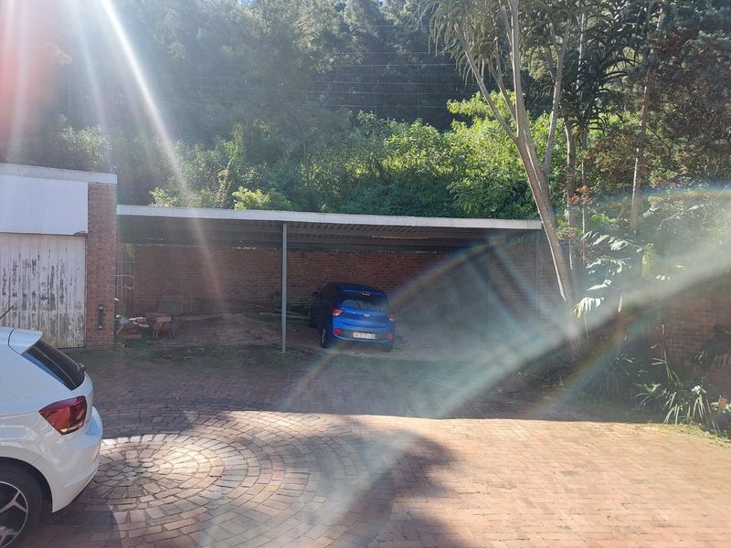 An outdoor carport area with brick paving and exposed brick walls, providing covered parking space.