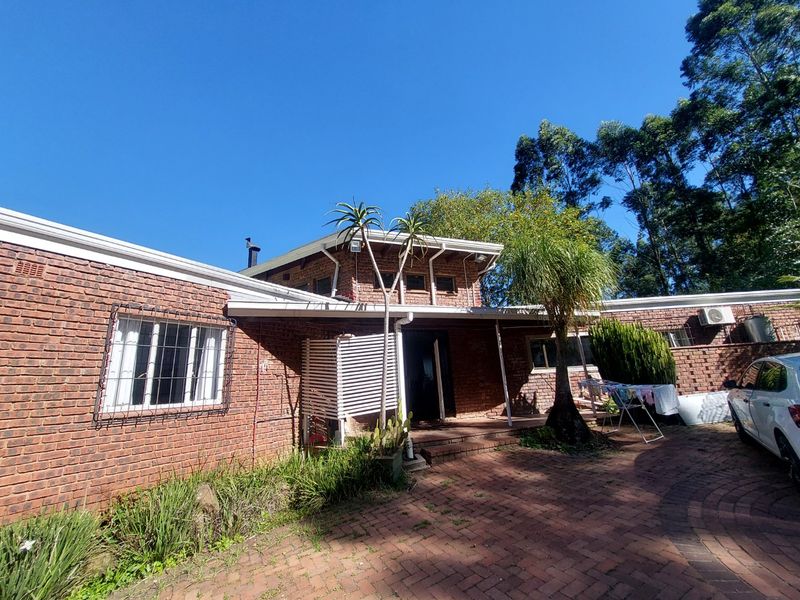Front elevation of a face brick house featuring a paved driveway, security bars on windows, and established garden surroundings.