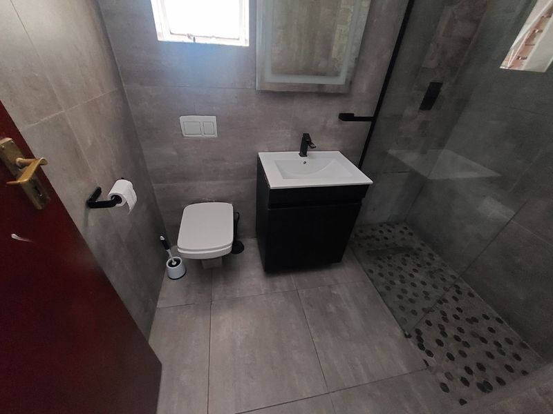 Modern bathroom featuring a wall-hung toilet, vanity basin, and a walk-in shower with a pebble-tiled floor and contemporary grey wall tiles.