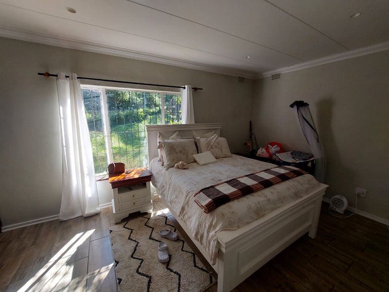 A bedroom featuring tiled flooring, recessed ceiling lighting, and a window fitted with security bars, offering natural light and a view of the garden.