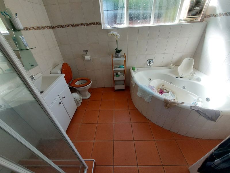 A functional bathroom featuring a corner spa bath, separate shower enclosure, vanity cabinet, and tiled finishes throughout.