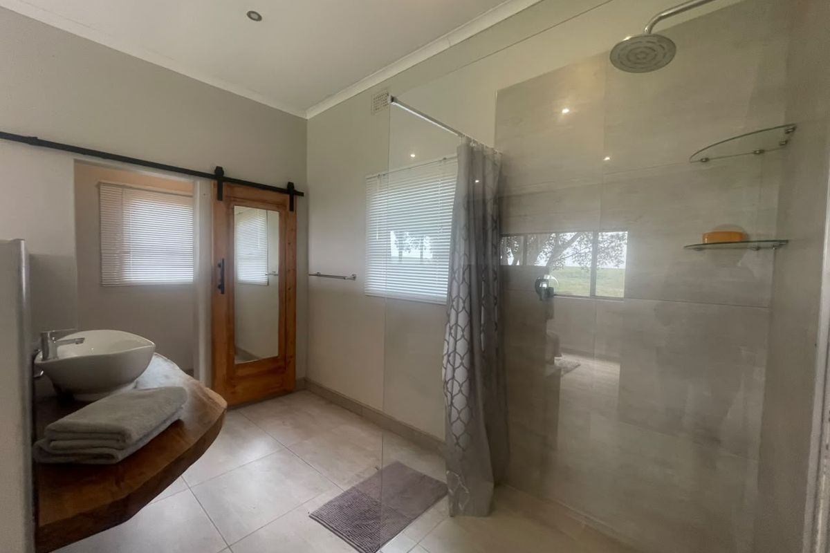 Modern bathroom featuring a spacious walk-in shower with glass screen, vessel sink on a natural wood vanity, and a stylish sliding barn door.