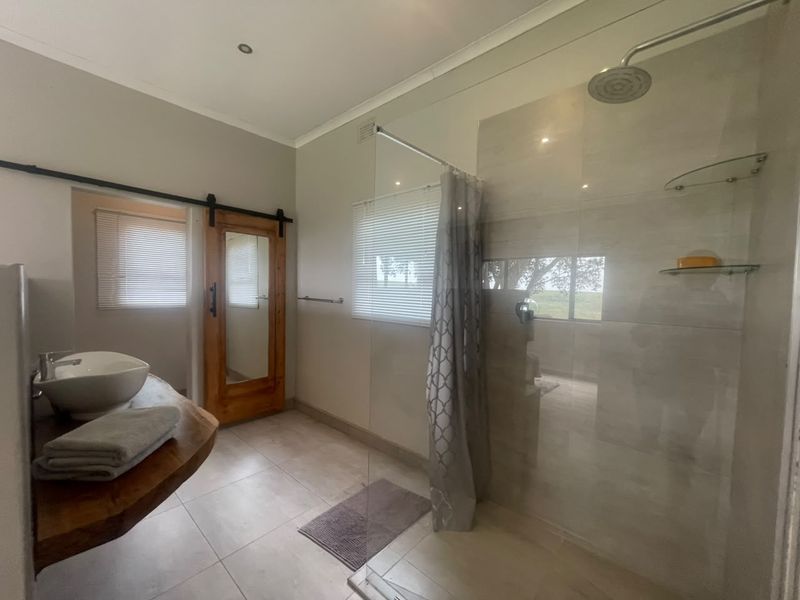 Modern bathroom featuring a spacious walk-in shower with glass screen, vessel sink on a natural wood vanity, and a stylish sliding barn door.