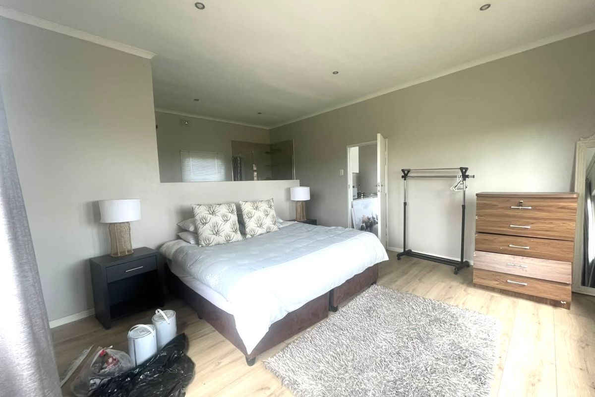 Spacious bedroom featuring light laminate flooring, recessed downlighting, and a large wall-mounted mirror reflecting the adjacent en-suite area.