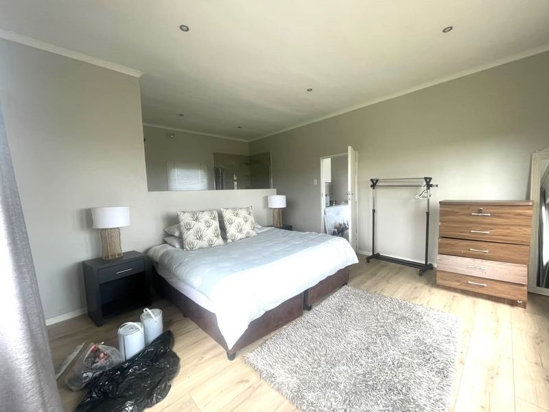 Spacious bedroom featuring light laminate flooring, recessed downlighting, and a large wall-mounted mirror reflecting the adjacent en-suite area.
