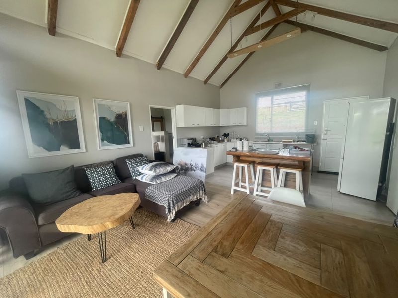 Open-plan living and kitchen area featuring vaulted ceilings with exposed timber beams, tiled flooring, and a functional kitchen island.