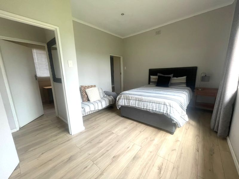 A well-lit bedroom featuring modern laminate flooring, neutral wall tones, and direct access to an adjoining room.