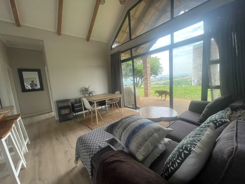 Spacious open-plan living area featuring vaulted ceilings with exposed timber beams, large windows providing natural light, and direct access to the outdoor patio.