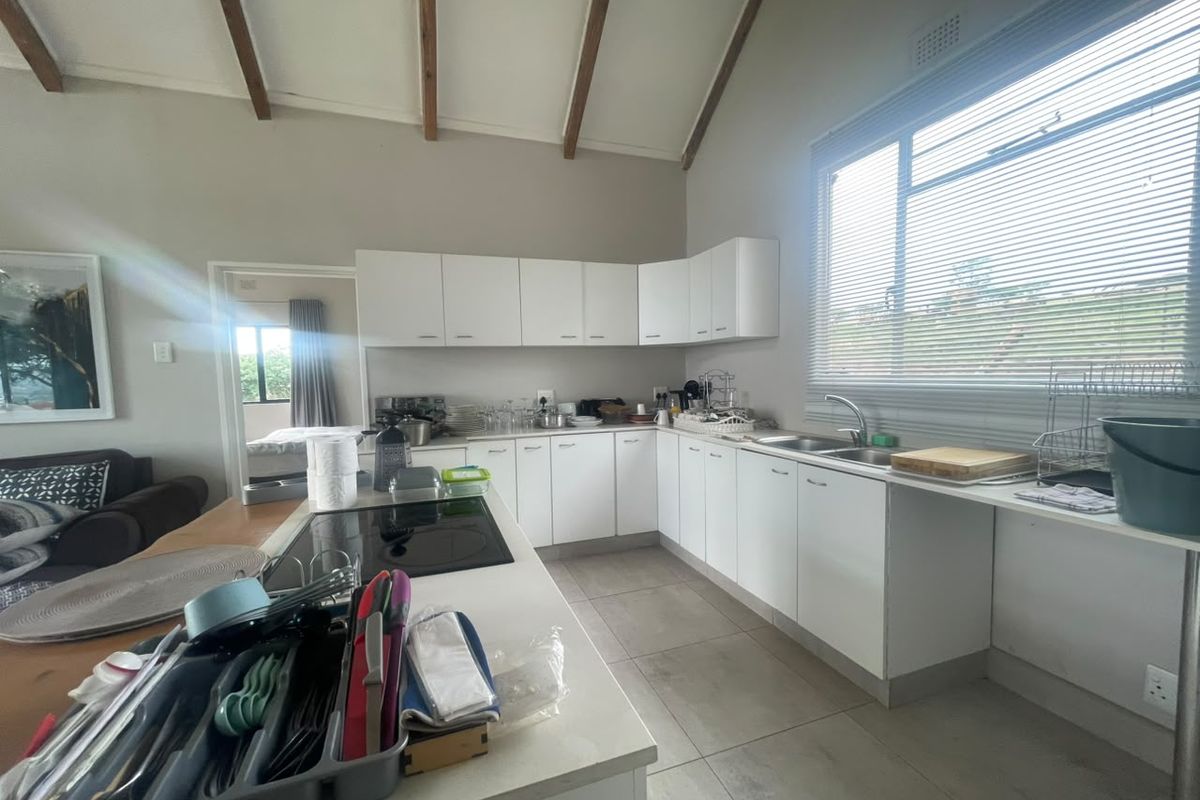 A functional kitchen featuring white cabinetry, a central island with an integrated hob, double sink, and exposed timber ceiling beams.