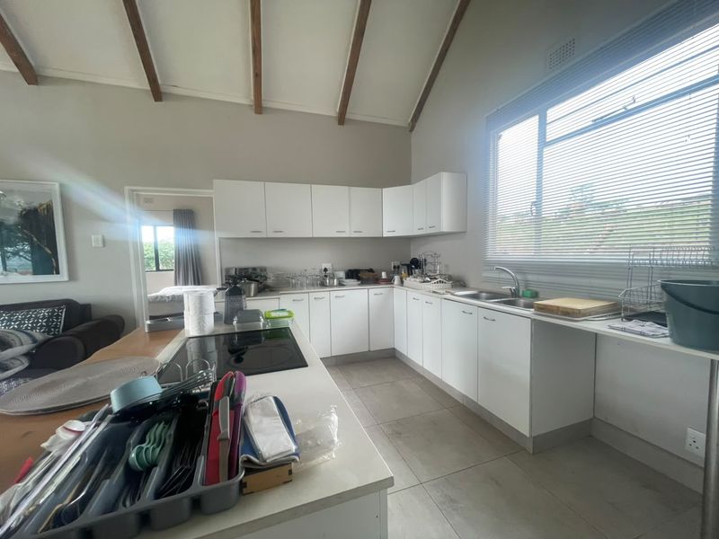 A functional kitchen featuring white cabinetry, a central island with an integrated hob, double sink, and exposed timber ceiling beams.