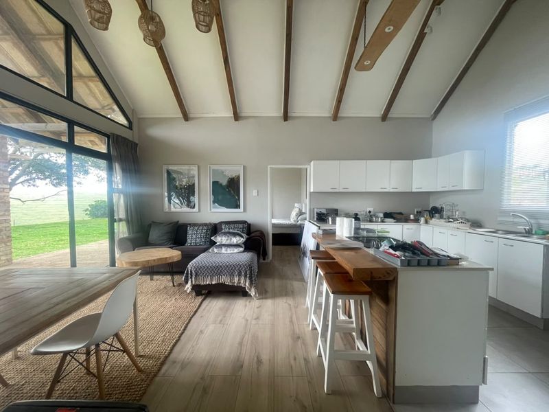 Spacious open-plan living and kitchen area featuring vaulted ceilings with exposed timber beams, modern white cabinetry, and large sliding doors leading to the outdoors.