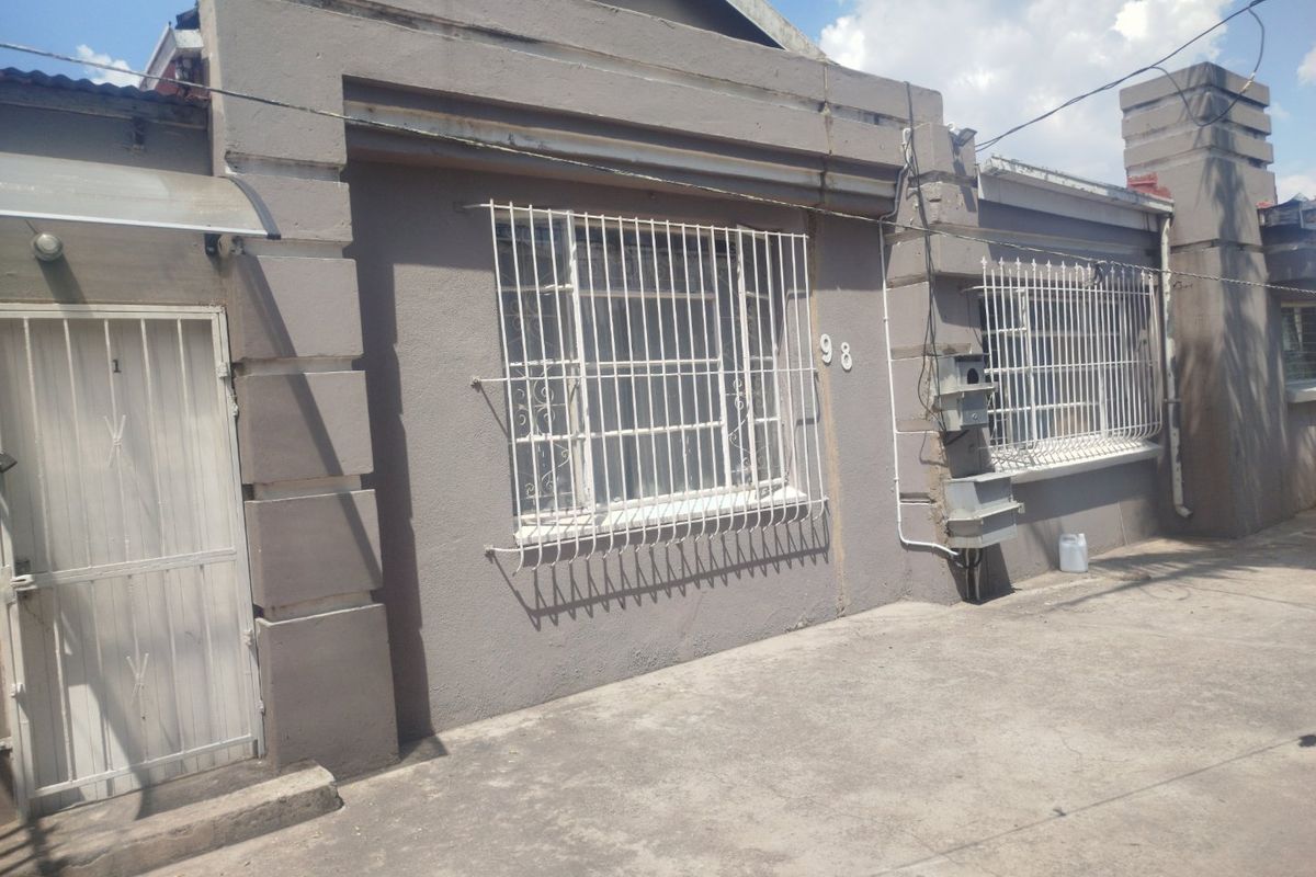 Front facade of a residential property featuring security bars on windows, a concrete driveway, and a secure entrance gate.