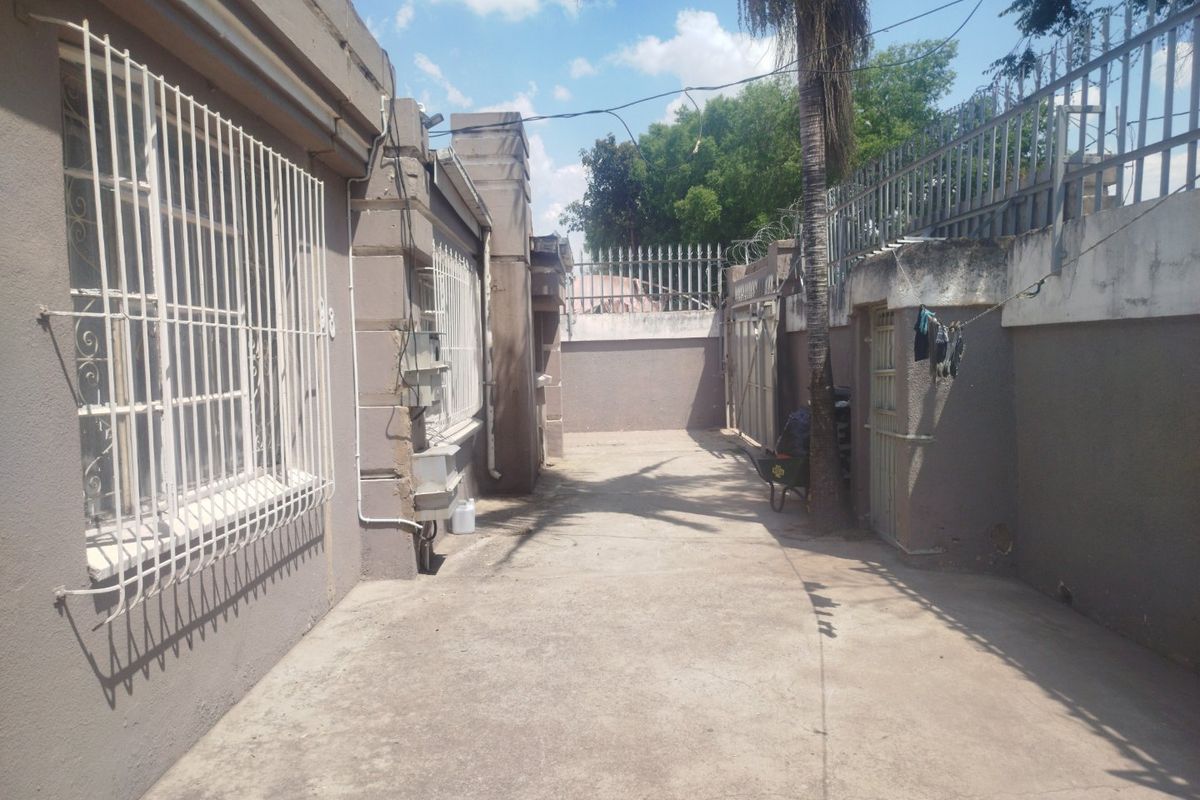 A paved rear exterior area featuring perimeter walls with security fencing and metal security bars on the windows.