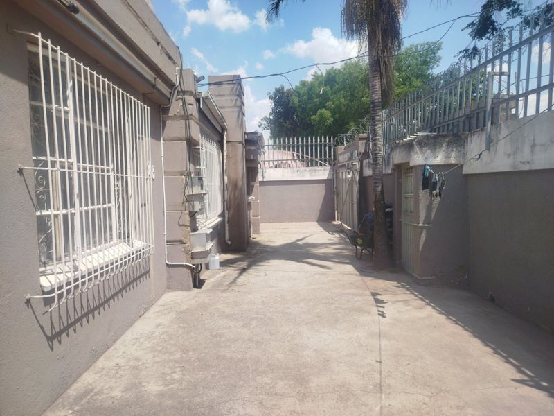 A paved rear exterior area featuring perimeter walls with security fencing and metal security bars on the windows.