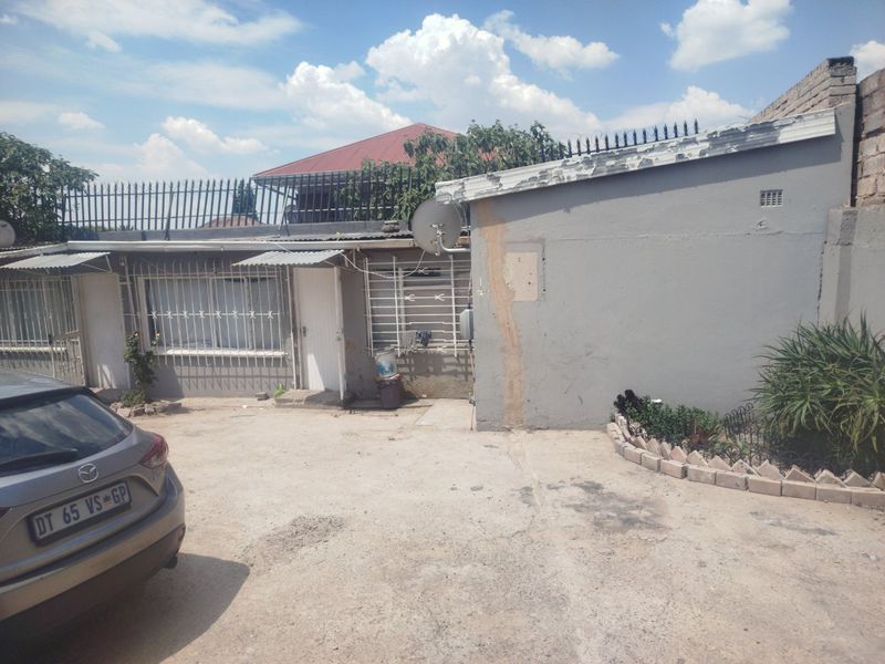 Front exterior view of the property featuring a concrete driveway, security bars on windows, and perimeter security spikes.