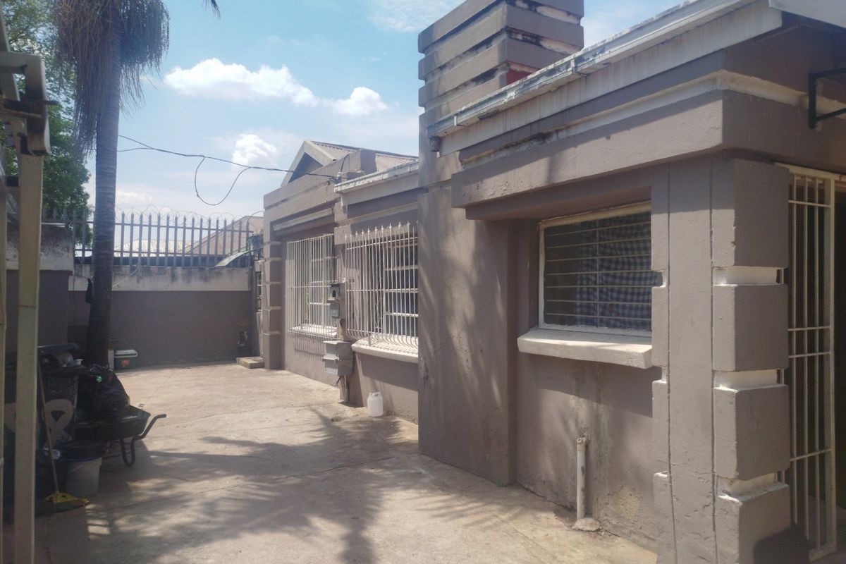 Rear exterior view of the property featuring concrete paving, security bars on windows, and a chimney stack, showing signs of wear on the exterior walls.