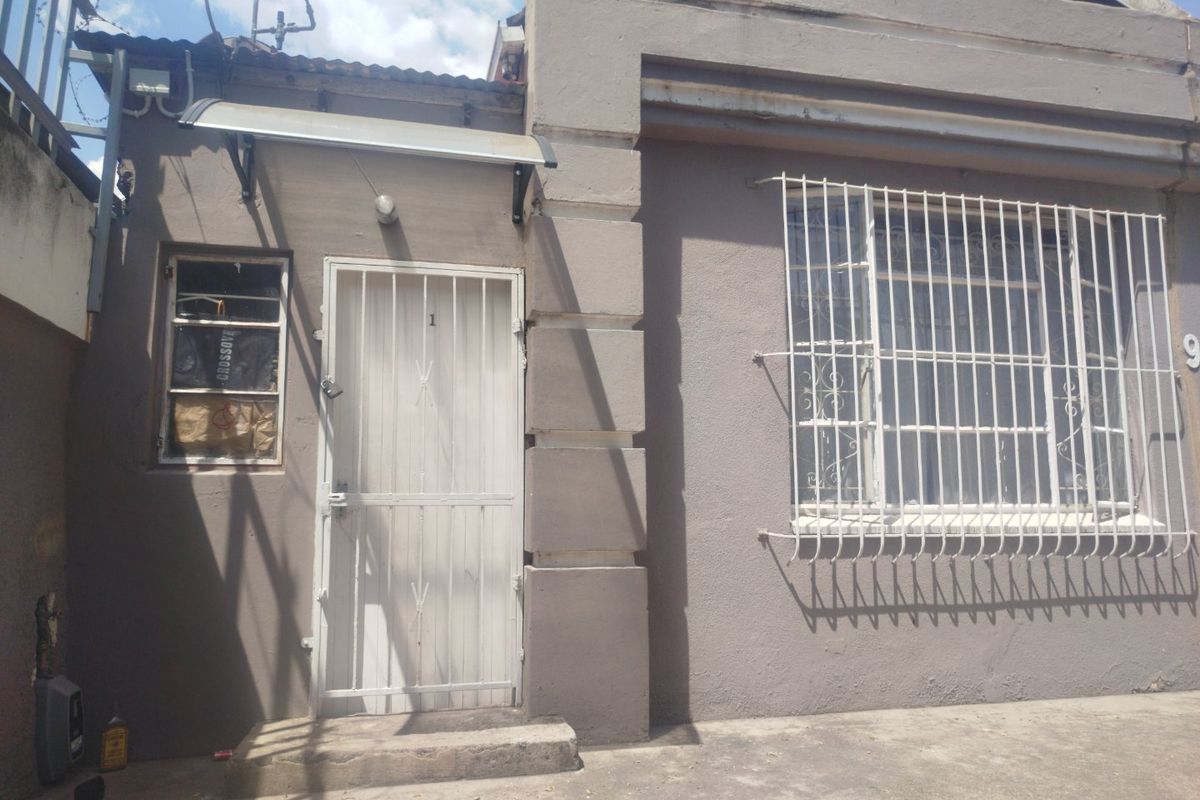 Front exterior view of the property featuring a security gate, protective window bars, and a concrete entrance area.