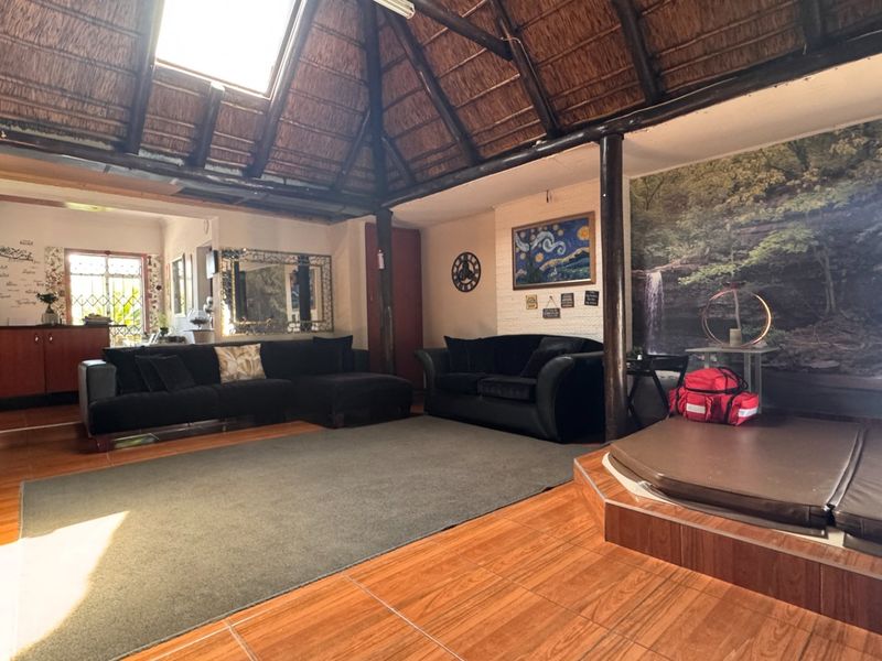 Spacious living area featuring a unique thatched roof with a skylight, exposed timber support poles, and a built-in raised platform area.