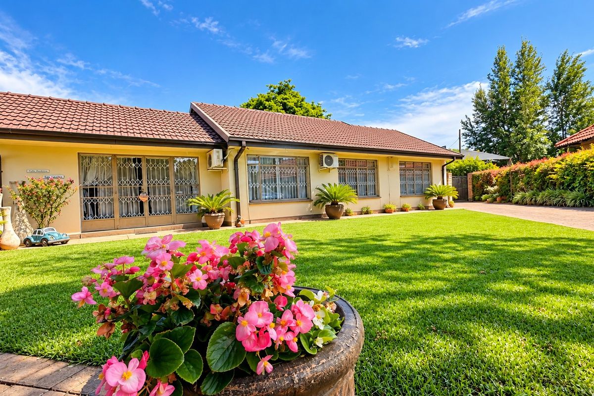 A well-maintained rear exterior view of the house featuring a spacious lawn, paved driveway, and secure access points with installed air conditioning units.