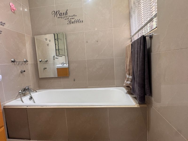 A functional bathroom featuring a built-in bathtub, wall-mounted vanity, and neutral wall tiling, providing a clean and practical space.