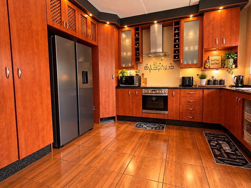 A well-maintained kitchen featuring warm-toned wooden cabinetry, integrated oven and extractor fan, dark countertops, and tiled flooring with a window security gate.