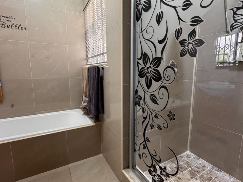 Modern bathroom featuring a built-in bathtub, separate shower enclosure with decorative glass, tiled finishes, and a vanity mirror.
