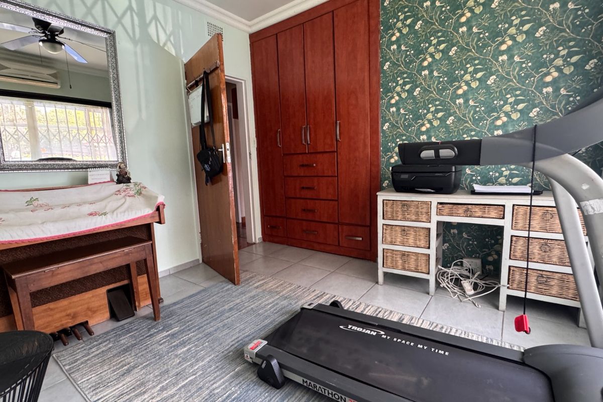 A bedroom featuring built-in wooden cabinetry, tiled flooring, and a ceiling fan, with patterned wallpaper accenting the wall.