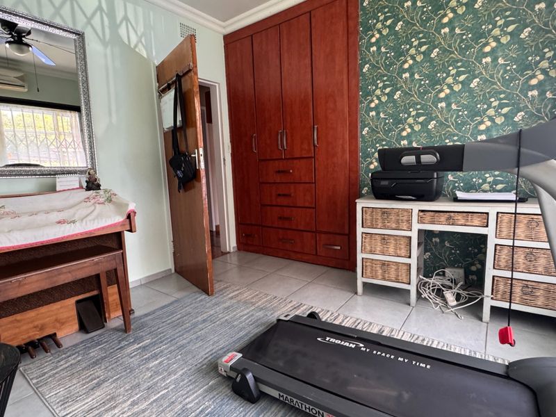 A bedroom featuring built-in wooden cabinetry, tiled flooring, and a ceiling fan, with patterned wallpaper accenting the wall.