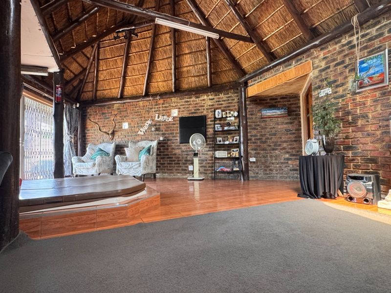 Spacious living area featuring a unique thatched roof, exposed brick walls, and a raised platform, offering a rustic and character-filled interior space.