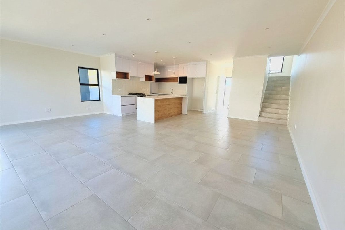 Spacious open-plan living area featuring a modern kitchen with a central island, tiled flooring, and an integrated staircase leading to the upper level.