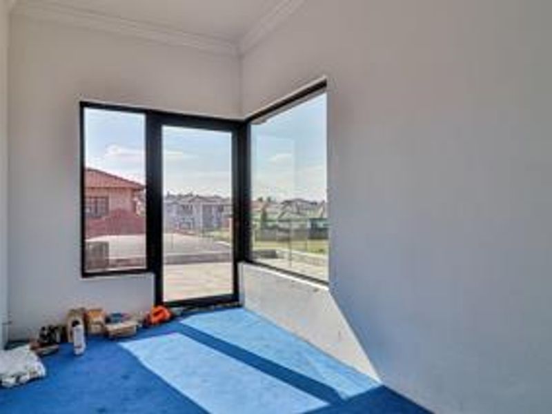 A bright, empty bedroom featuring large corner windows and a glass door providing access to an outdoor area.