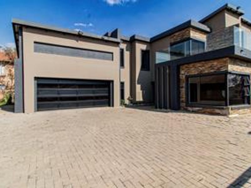 Modern double-story residence featuring a paved driveway, integrated double garage, and contemporary architectural elements including stone cladding and glass balcony railings.