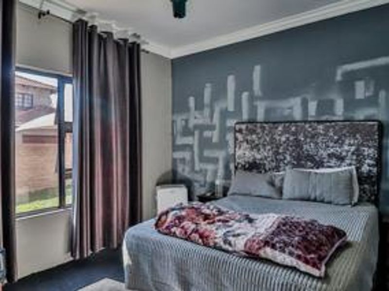 A bedroom featuring a large window with curtains, a ceiling fan, and a decorative painted feature wall.