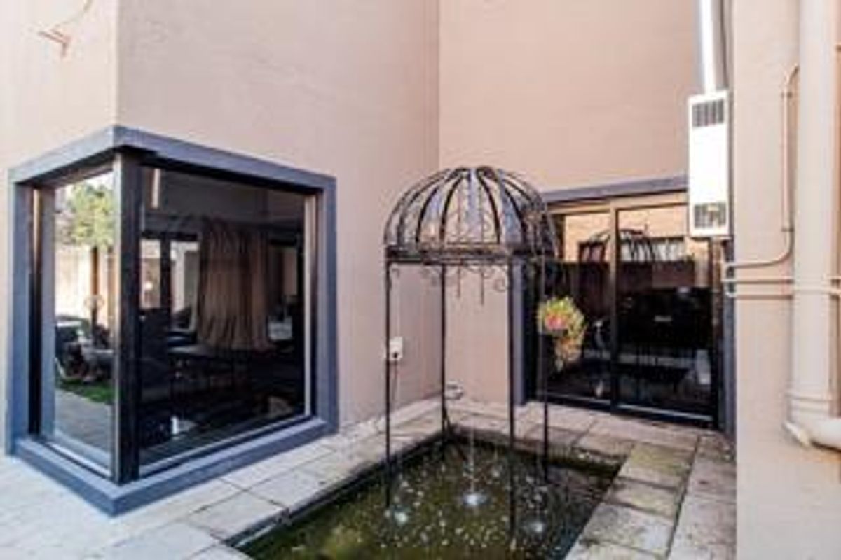Rear courtyard area featuring a decorative metal water fountain, paved flooring, and large sliding glass doors providing access to the interior living space.