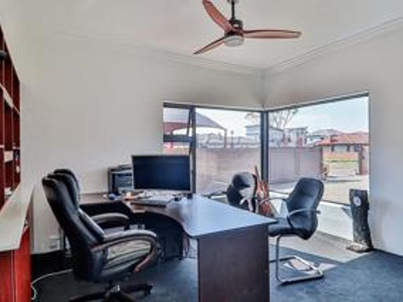 A functional home office featuring built-in shelving, a ceiling fan, and large corner windows providing ample natural light.