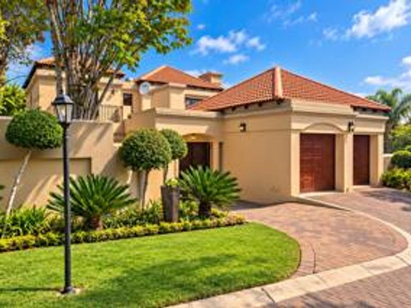 A well-maintained front elevation featuring a paved driveway, double garage, and manicured garden with established landscaping and exterior lighting.