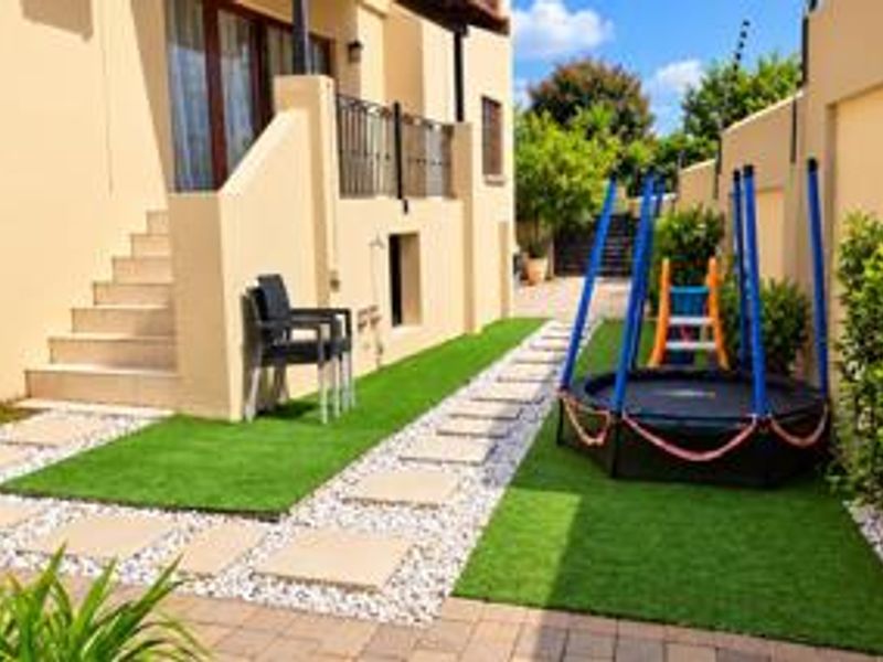 A well-maintained rear garden area featuring artificial lawn, stone paving pathways, and a concrete staircase leading to the upper level of the house.