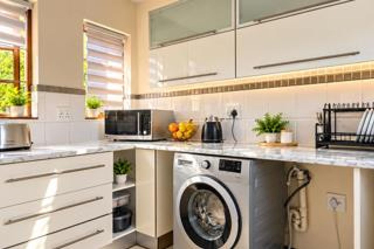 A well-maintained kitchen featuring modern white cabinetry, marble-look countertops, tiled backsplash, and integrated laundry plumbing.