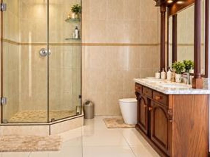 A well-maintained bathroom featuring a glass shower enclosure, a classic wooden dual-sink vanity with a marble countertop, and neutral floor-to-ceiling tiling.