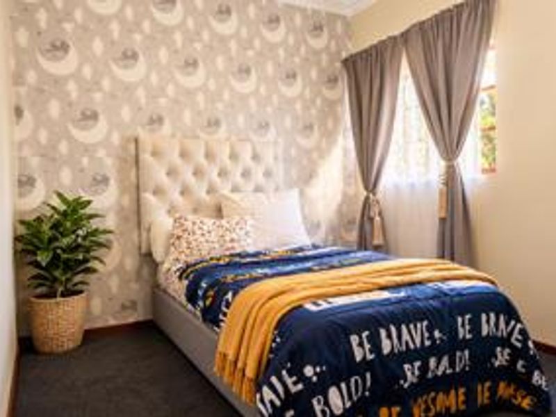 A cozy bedroom featuring patterned wallpaper, carpeted flooring, and a window with curtains, providing a comfortable and well-maintained living space.